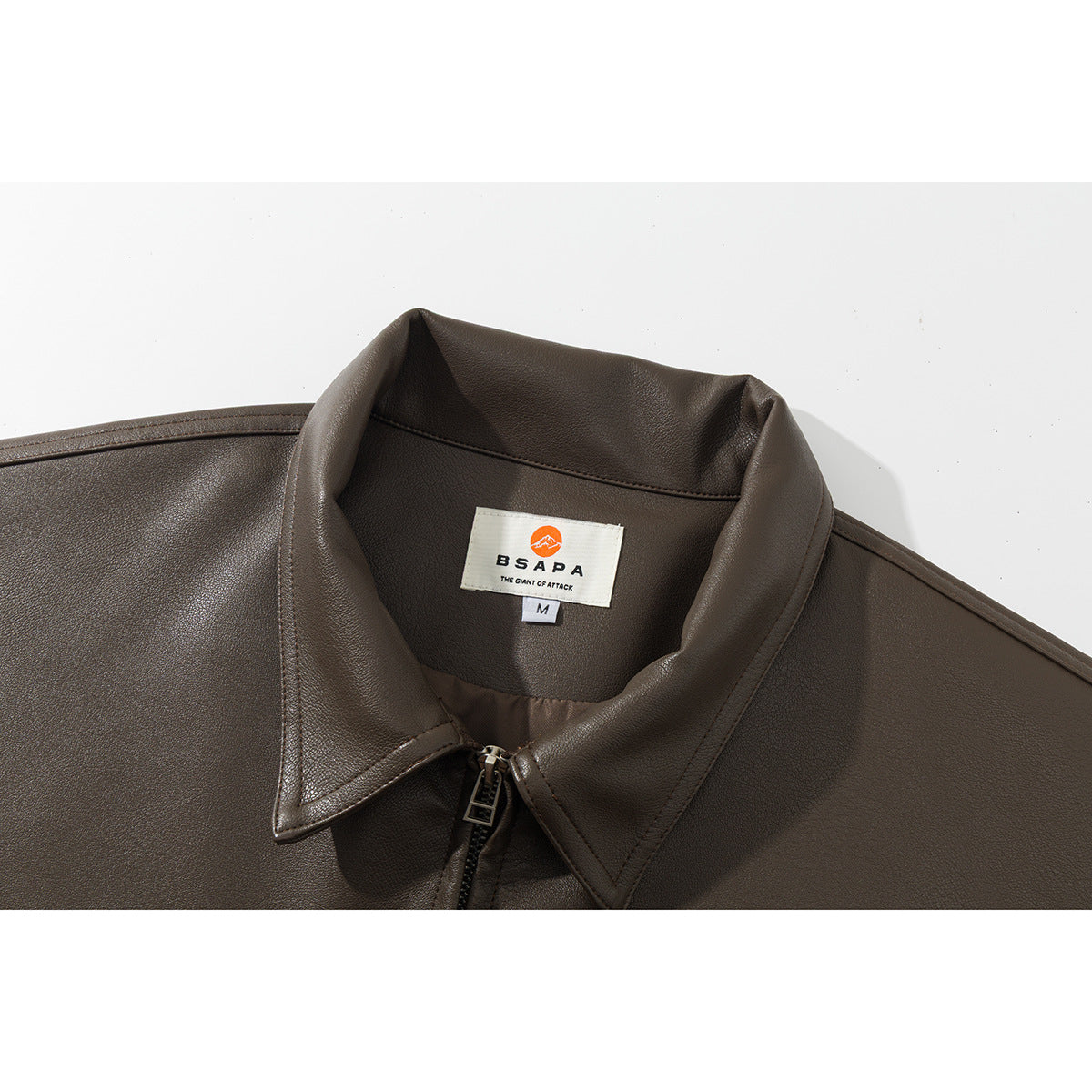 Close-up of a dark brown jacket’s pointed collar, front zipper, and sewn neck label.