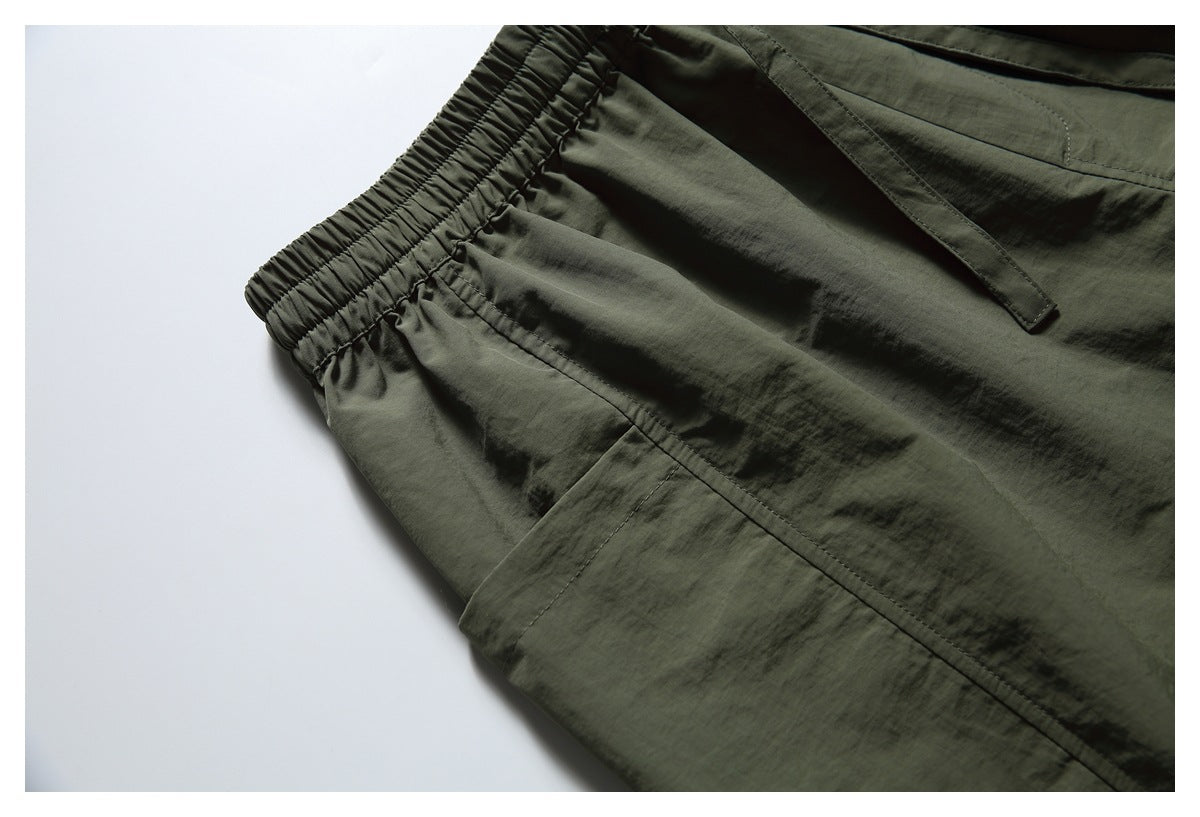 Angled close-up of olive shorts showing the elastic waistband, drawstring and side pocket.