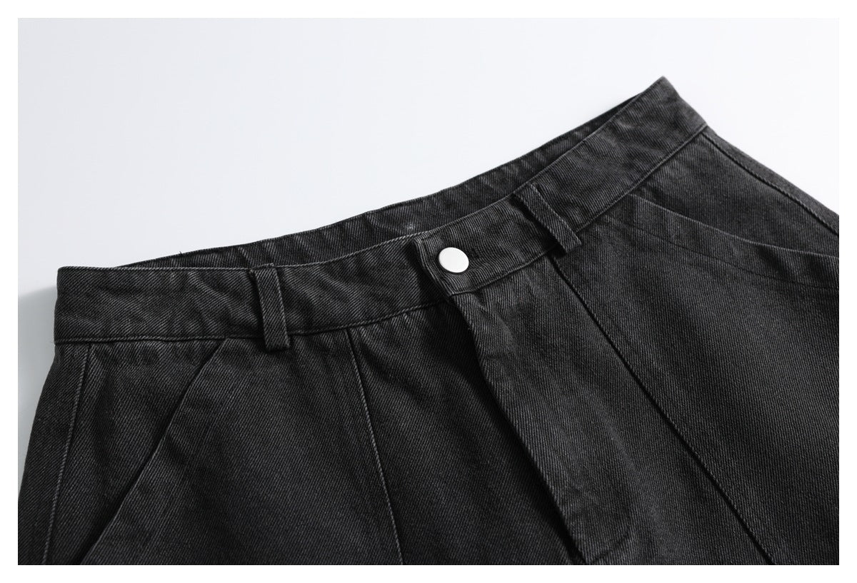 Close-up of charcoal-black denim trousers showing the waistband, belt loop, silver button and front pleats.