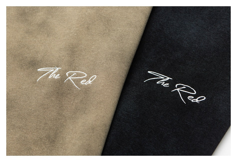 Close-up of tan and charcoal sweatshirt fabric, each embroidered with white script reading “The Red.”