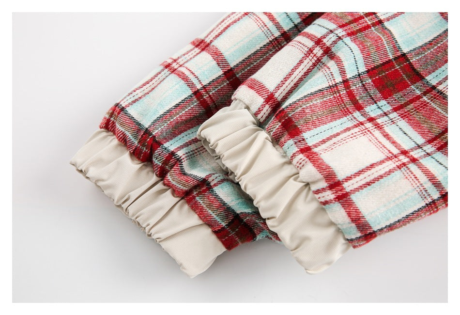 Close-up of gathered cream fabric trim at the ends of red, cream, and pale blue plaid garment pieces.