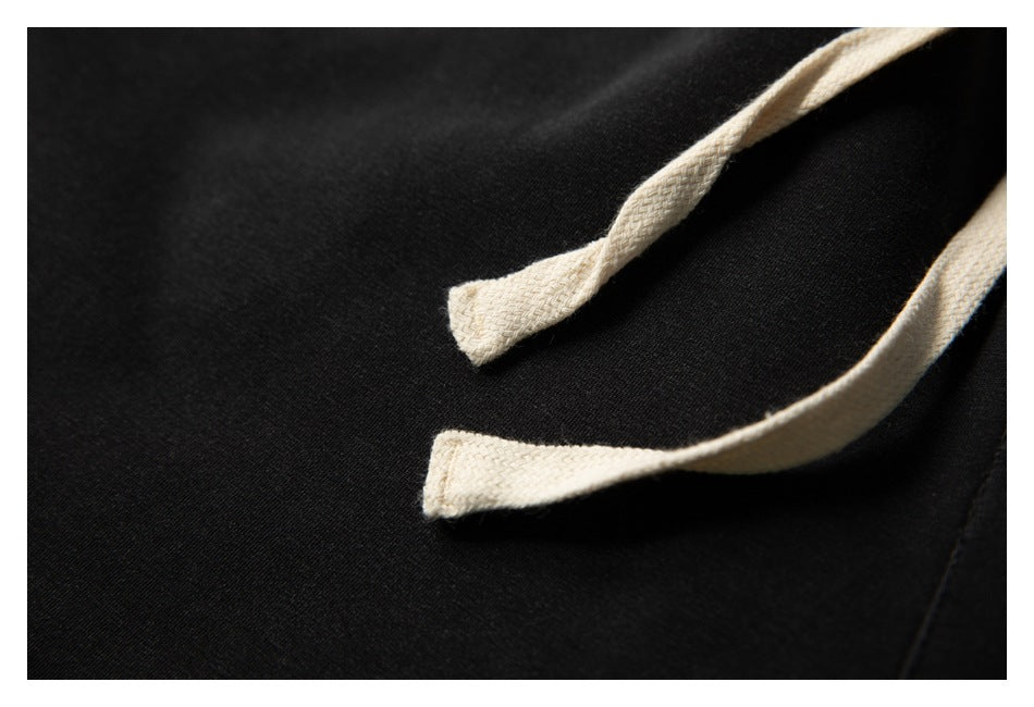Close-up of two cream drawstring ends against black jogger pants.