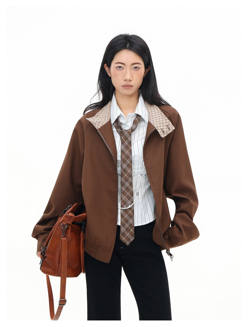 Model in open brown stand-collar jacket with plaid collar, striped shirt, tie and a brown leather bag