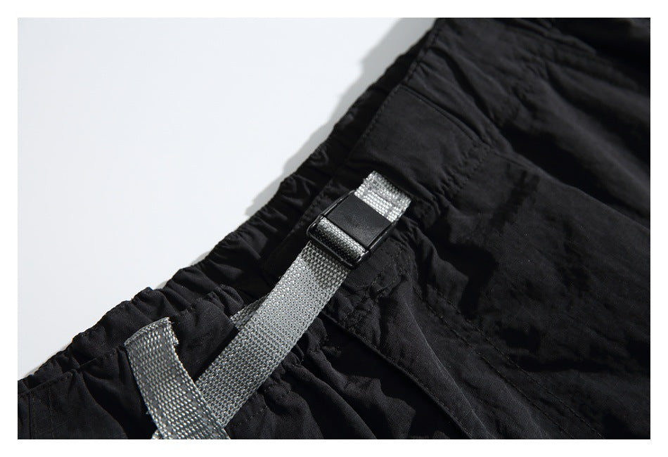 Close-up of the gray webbing belt and black buckle on the elastic waist of black pants.