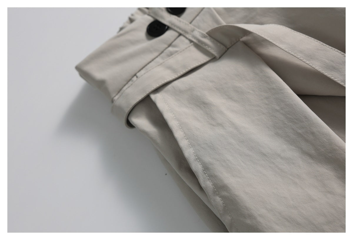 Close-up of a light taupe garment showing a belt loop, waistband buttons, and a stitched pocket edge.