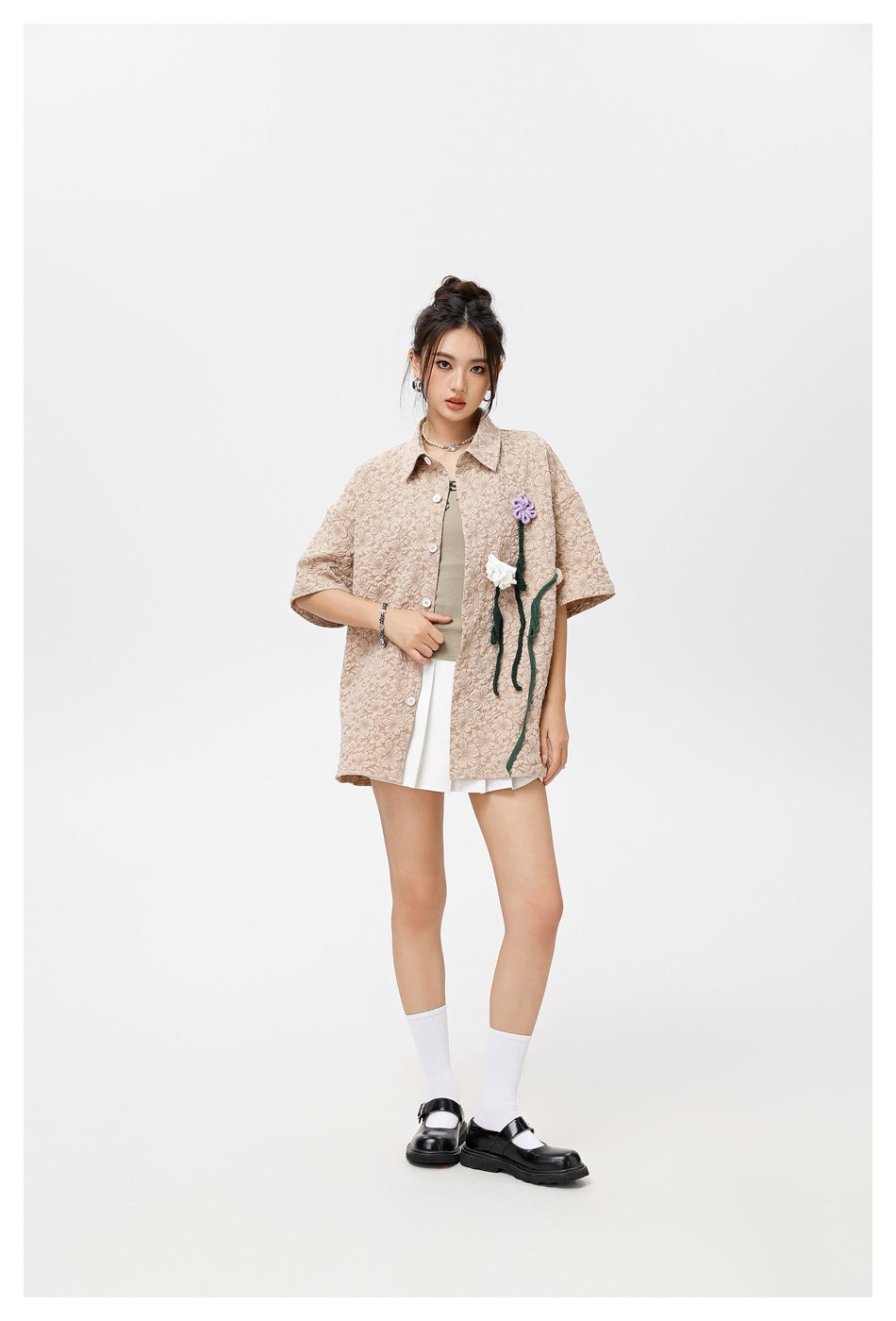 Model wearing the khaki floral textured shirt open over a tank top and white pleated skirt, standing front view