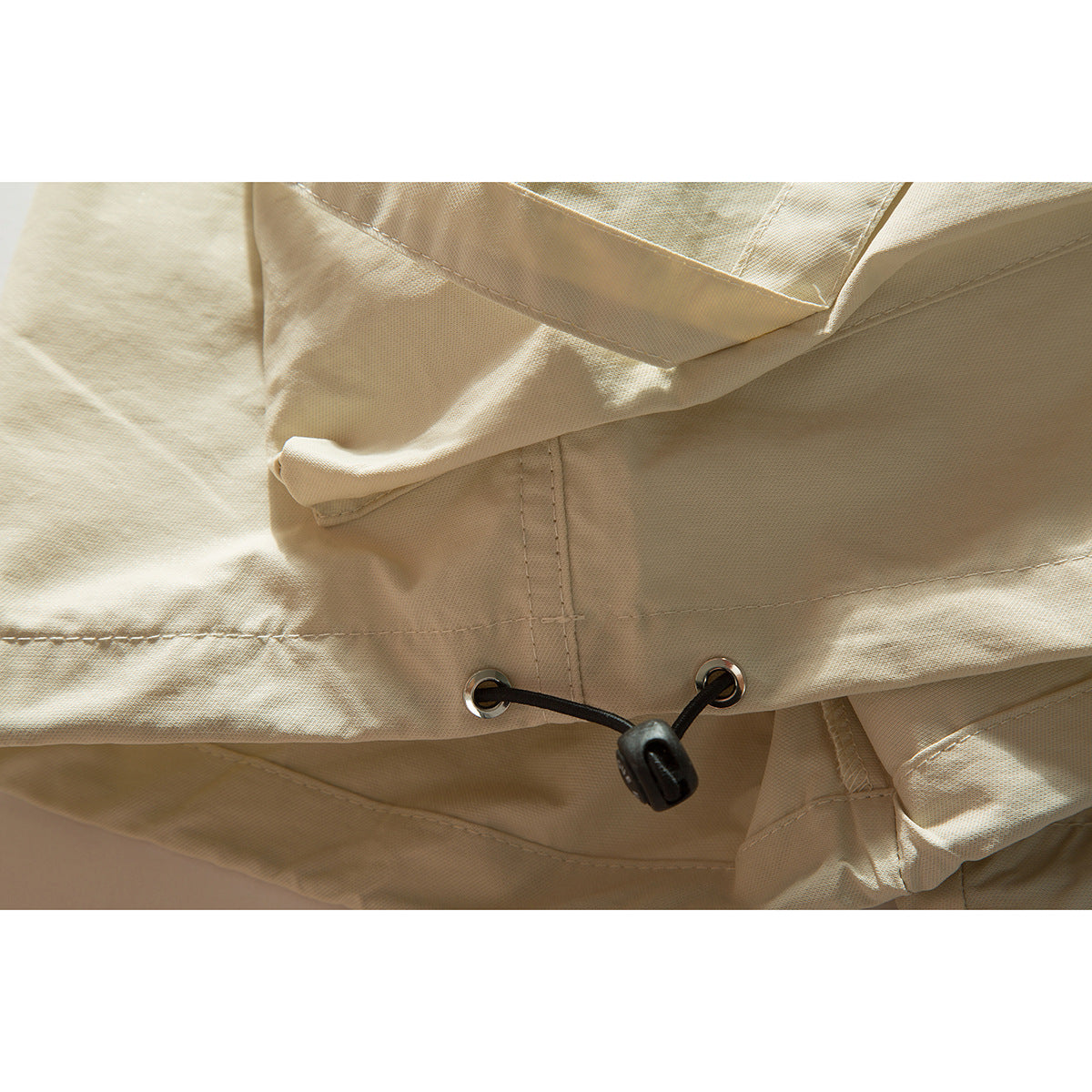 Close-up of the cream shorts' hem, showing a metal eyelet and black drawcord toggle.