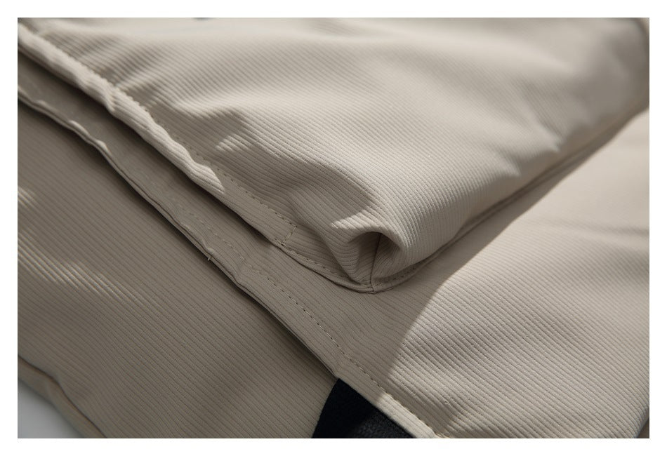 Close-up of beige ribbed jacket fabric, showing a stitched folded edge and seam.