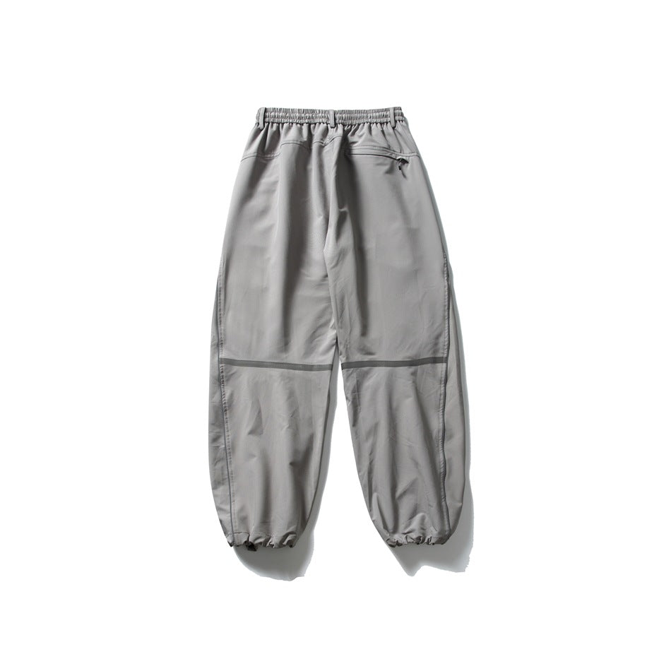 Light gray loose-fit pants shown from the back, with an elastic waist, zip pocket, reflective knee bands and gathered cuffs.