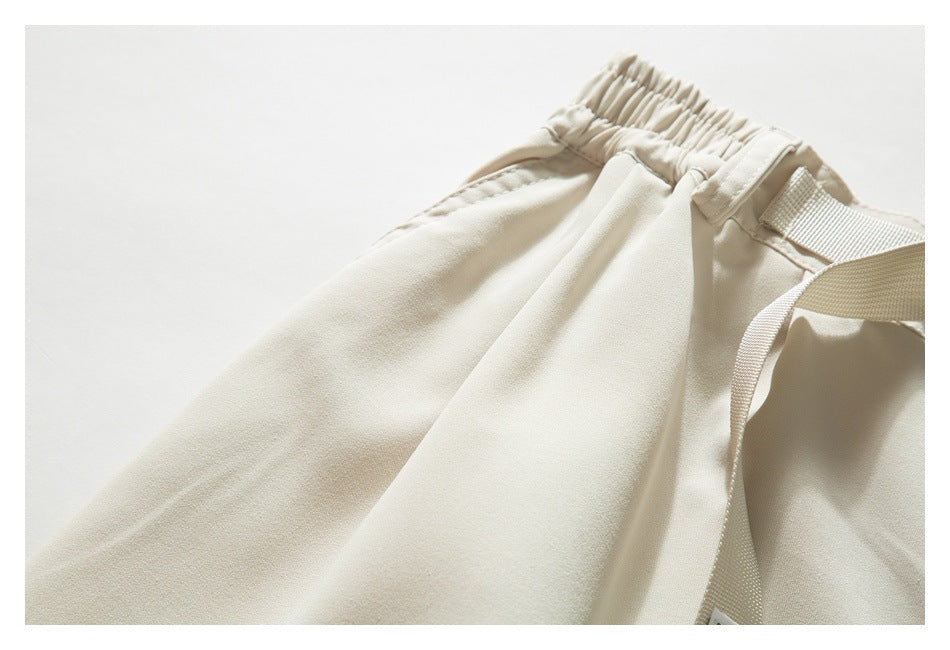 Close-up of the beige shorts' elastic waistband, belt loop, and adjustable webbing belt.