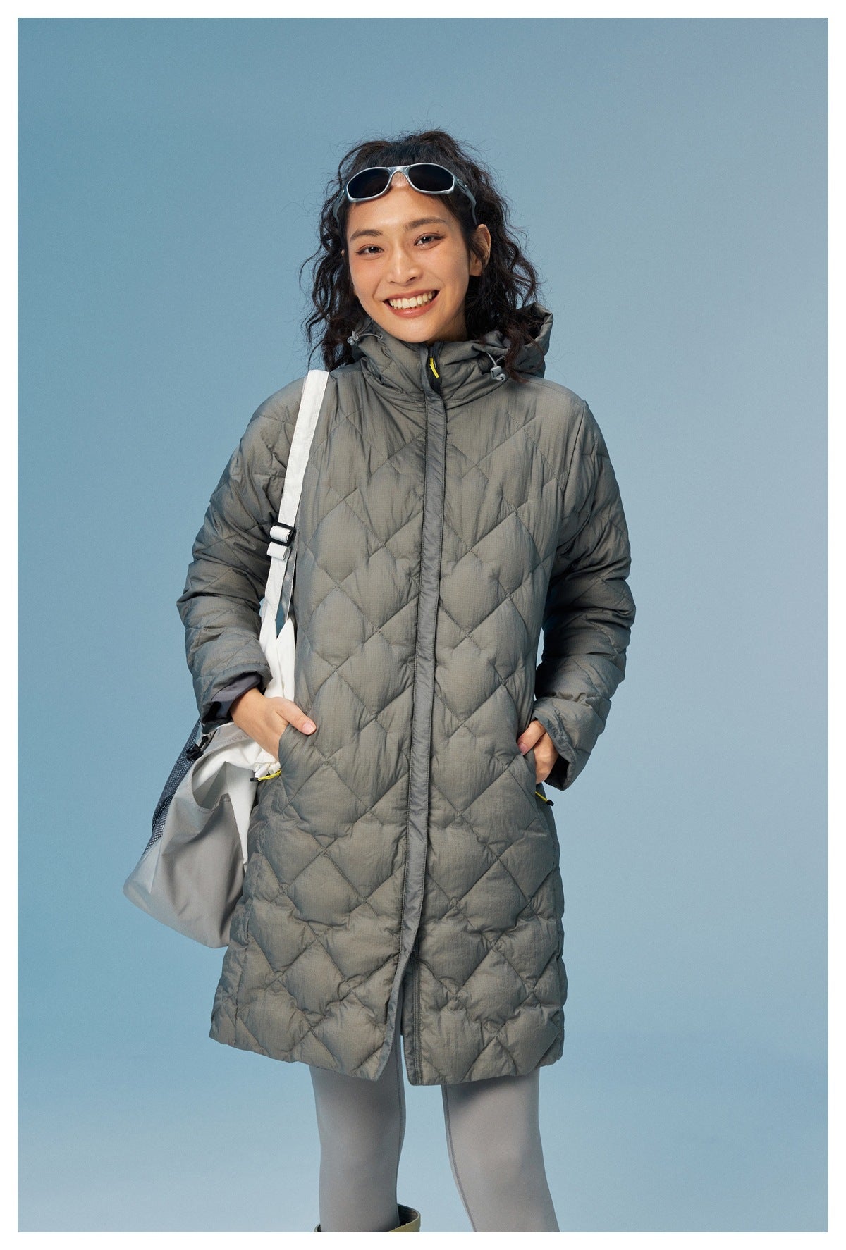 Model wearing a long gray diamond-quilted hooded coat with a front zip and pockets.