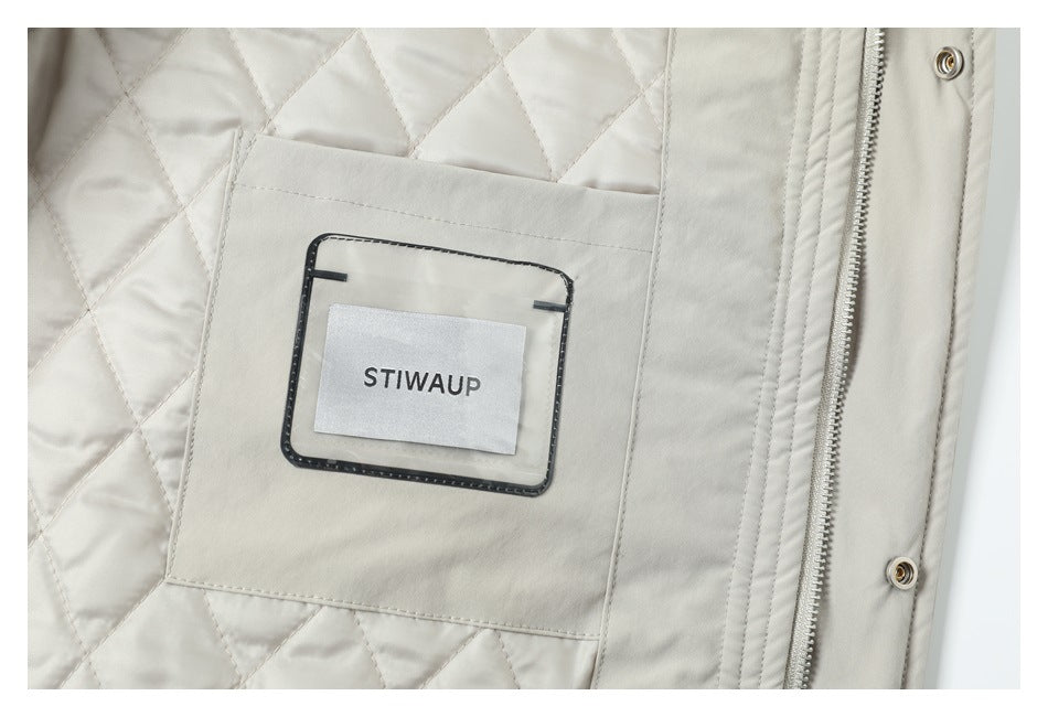 Close-up of a light beige quilted jacket interior showing a sewn-in STIW AUP label, zipper, and snap fasteners.