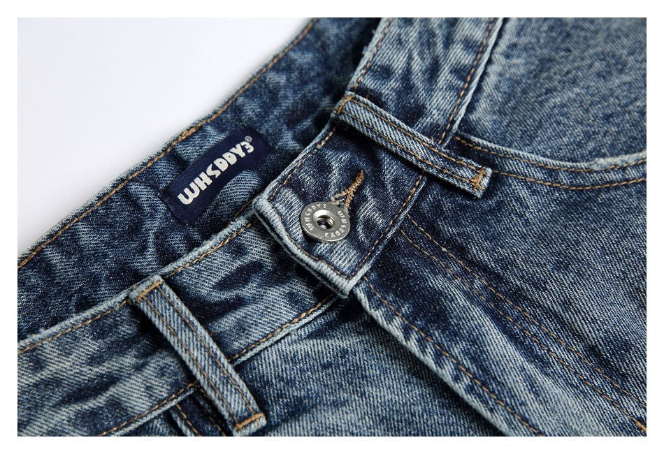 Close-up of the blue denim waistband, metal button, belt loop, and sewn-in English brand label.