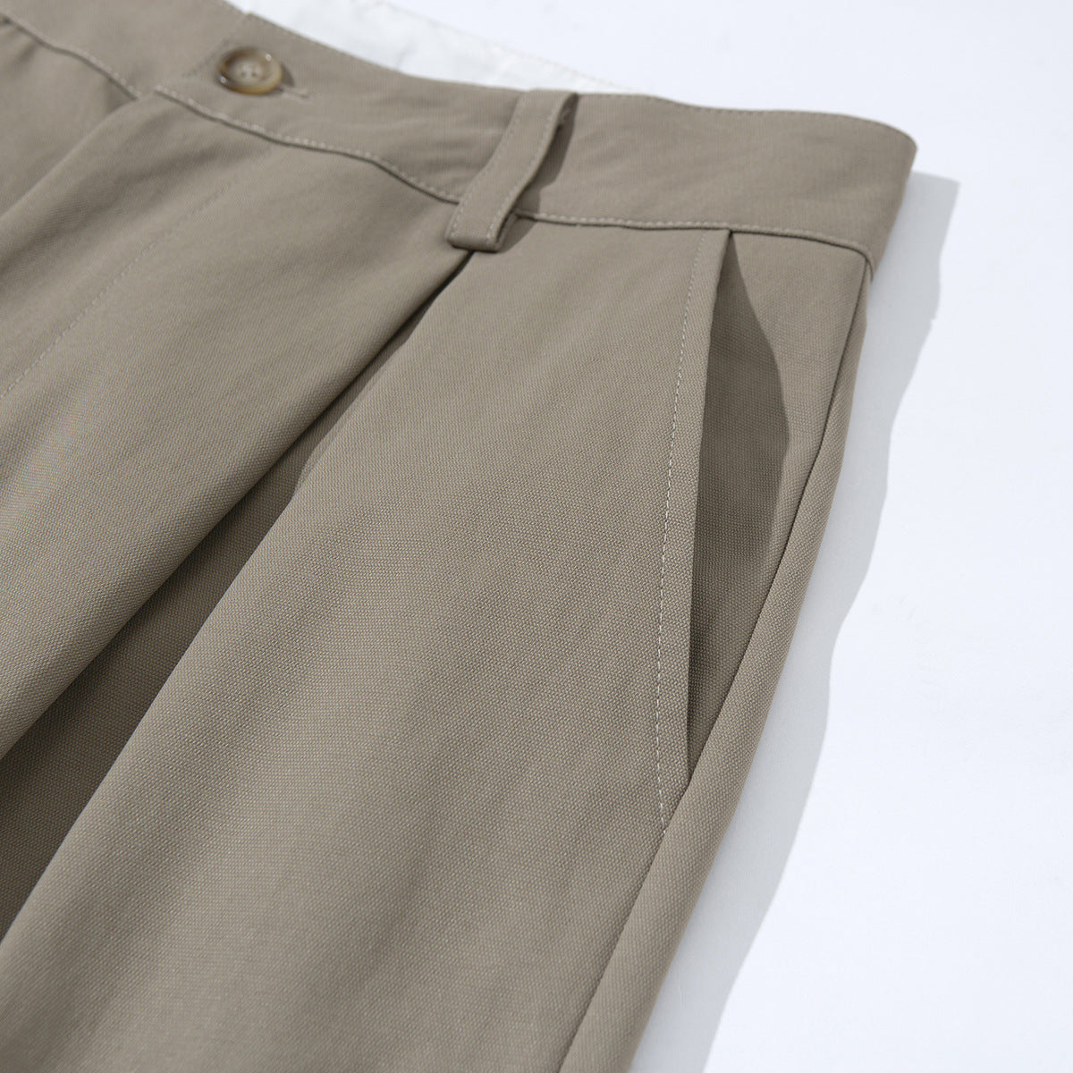 Angled close-up of taupe tailored shorts highlighting a belt loop, front pleat, and side seam.