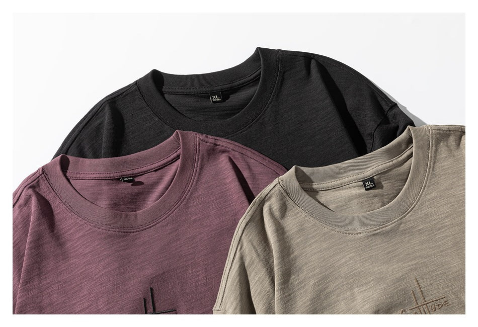 Three T-shirts in black, muted mauve, and beige-gray, shown overlapping at the crew necks.