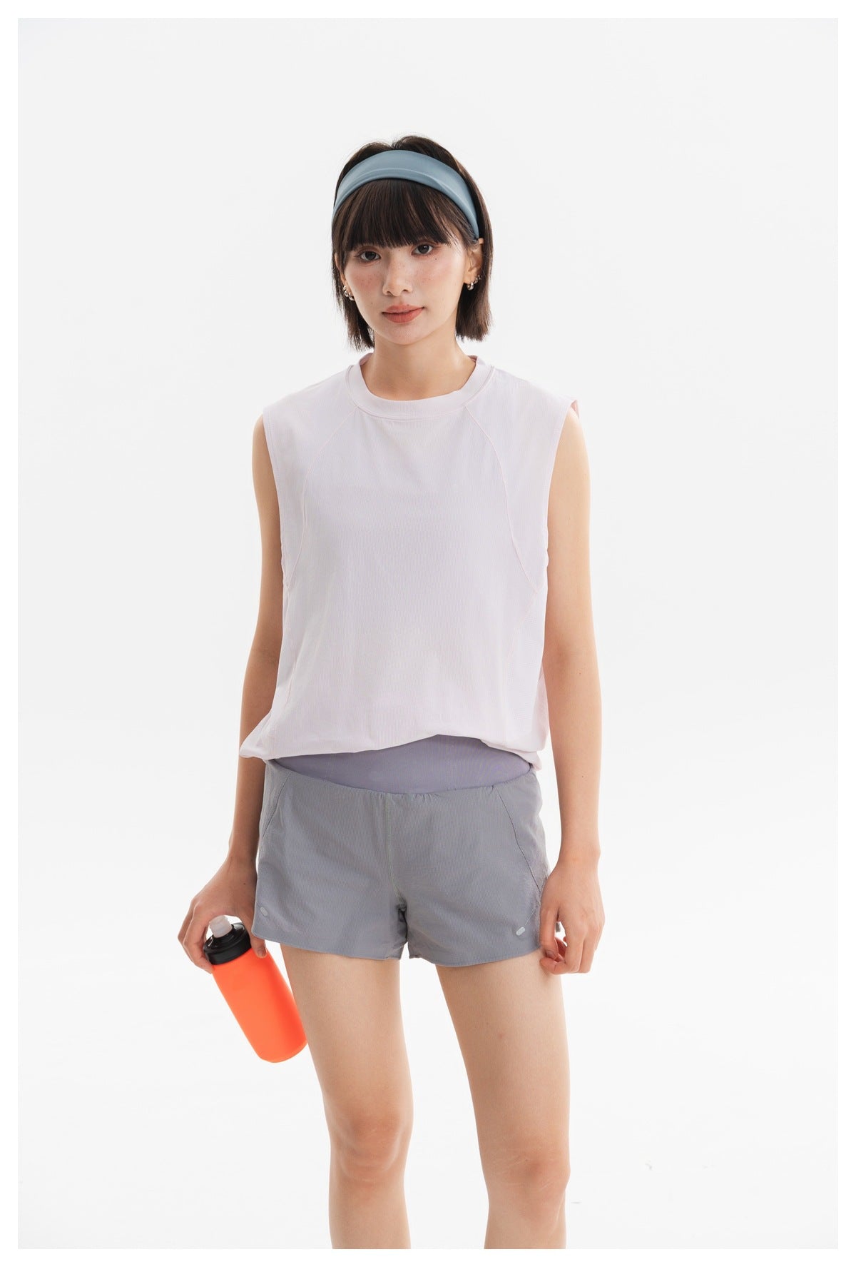 Front view of a model wearing a pale pink sleeveless athletic top and gray running shorts in a bright studio.