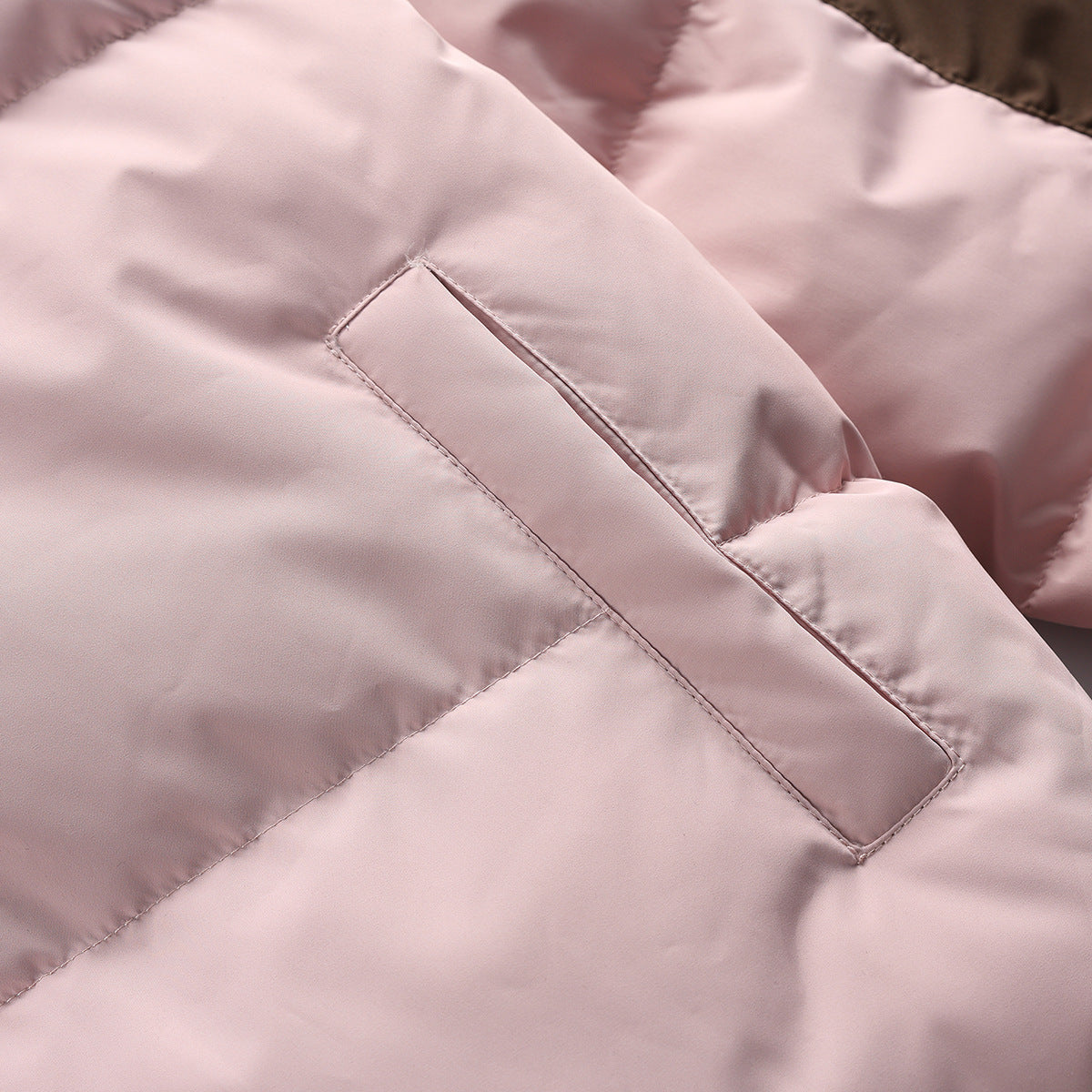 Close-up of the pale pink puffer jacket fabric and diagonal welt pocket opening.