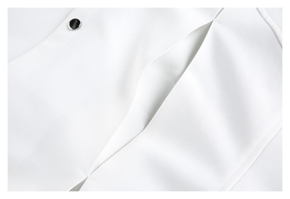 Close-up of a white garment showing a dark snap button and a folded seam or pleat.