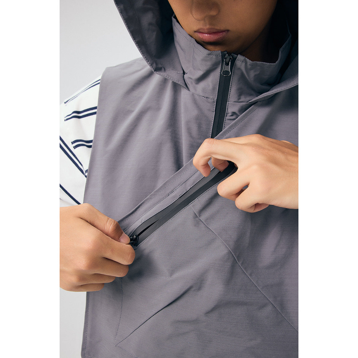Close-up of the gray vest showing its hood, front zipper, and diagonal zip pocket being opened.