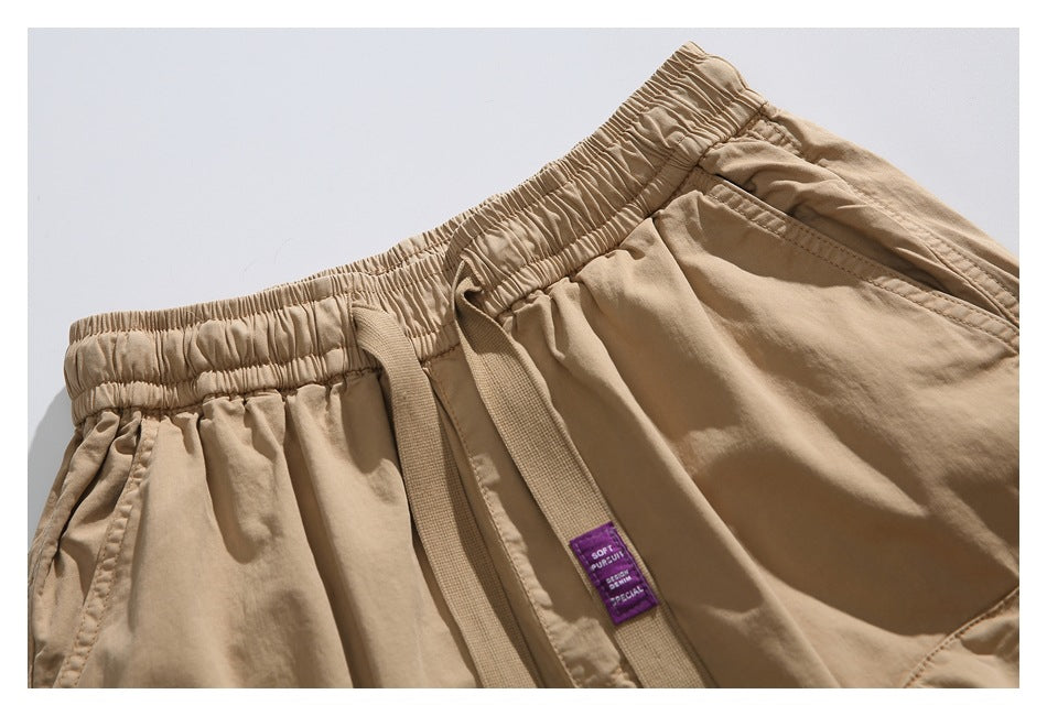 Close-up of tan shorts showing the gathered elastic waistband, drawstring, and a small purple sewn-in label.