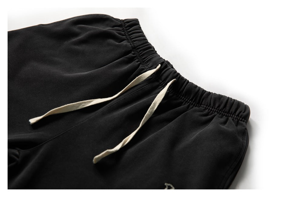 Close-up of black jogger pants showing a gathered elastic waistband and two cream drawstrings.