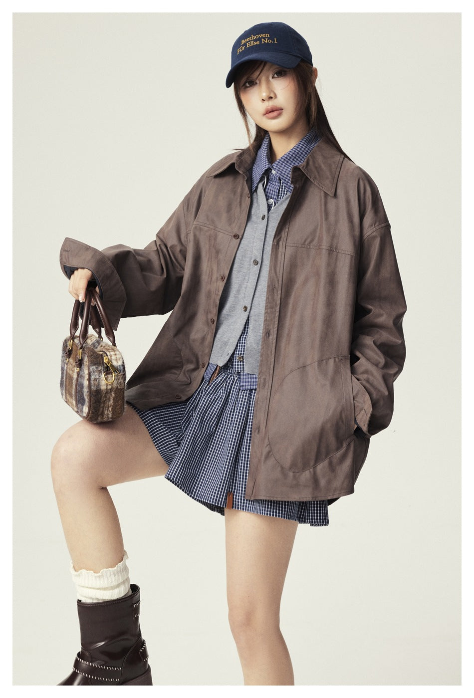 Model wearing a brown oversized jacket over a blue checked outfit, shown with the jacket's front and patch pockets.