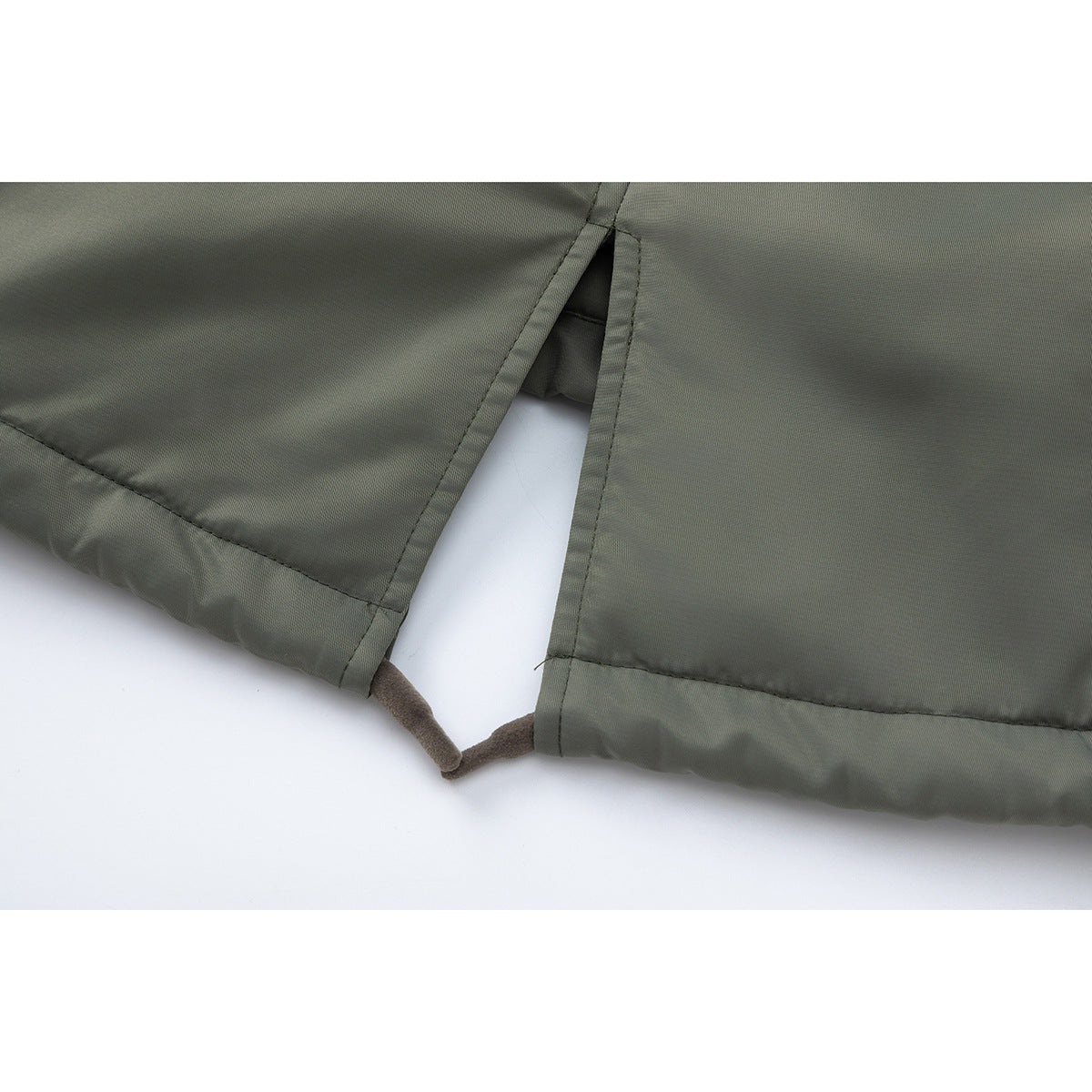 Close-up of an olive-green jacket hem with a split opening and a short brown loop between the edges.