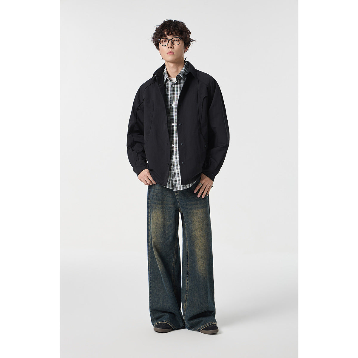 Model wearing a black collared snap-front jacket over a plaid shirt and wide-leg jeans.