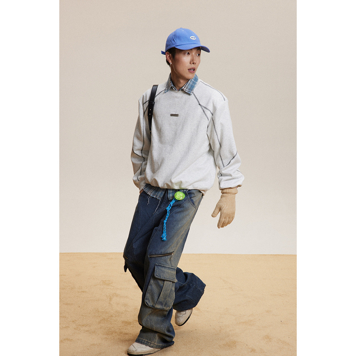 Model wearing a light gray sweatshirt with dark contrast seams, plaid shirt, and loose dark cargo jeans.