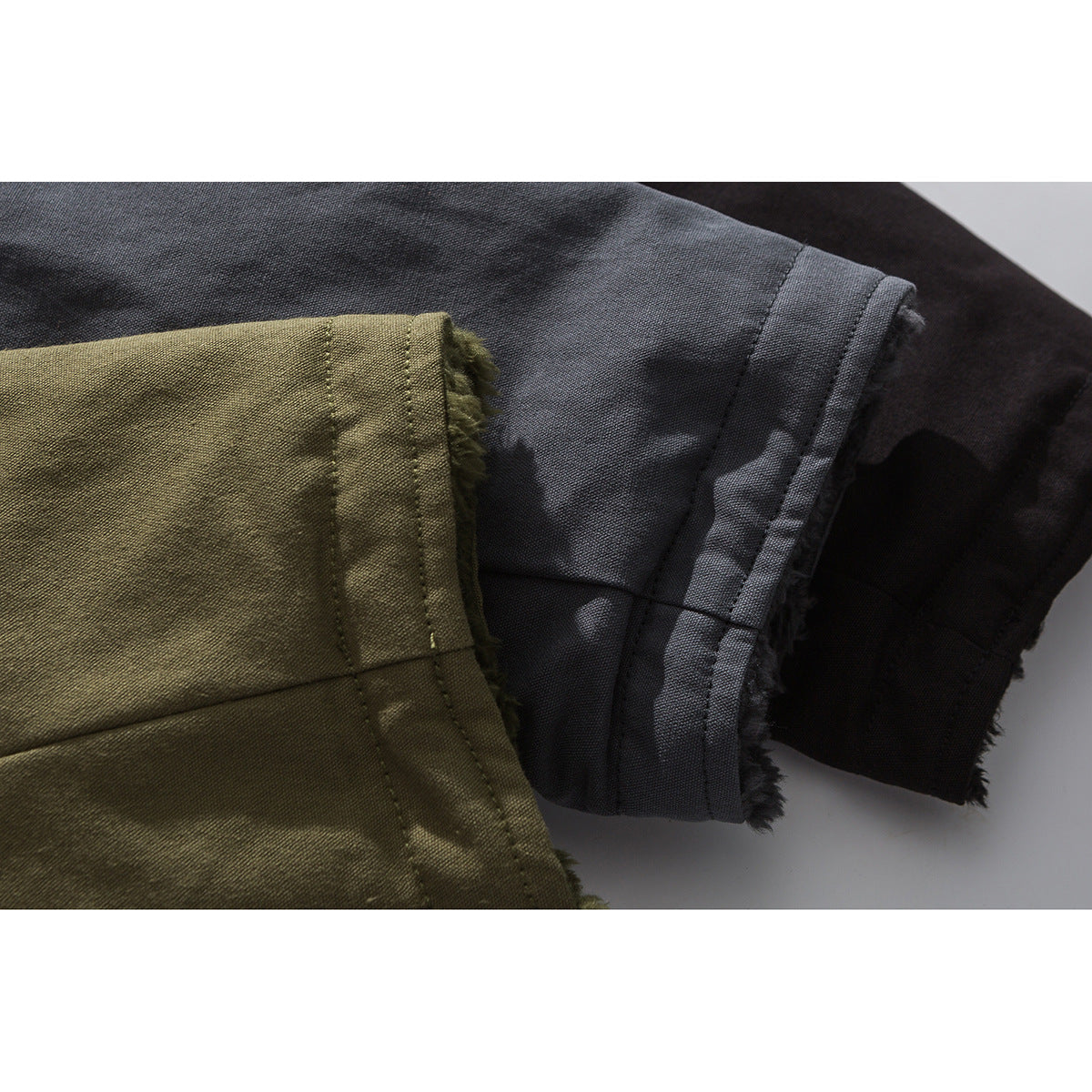 Close-up of coat sleeve cuffs in olive, charcoal, and black, showing the fabric edges and fuzzy lining.