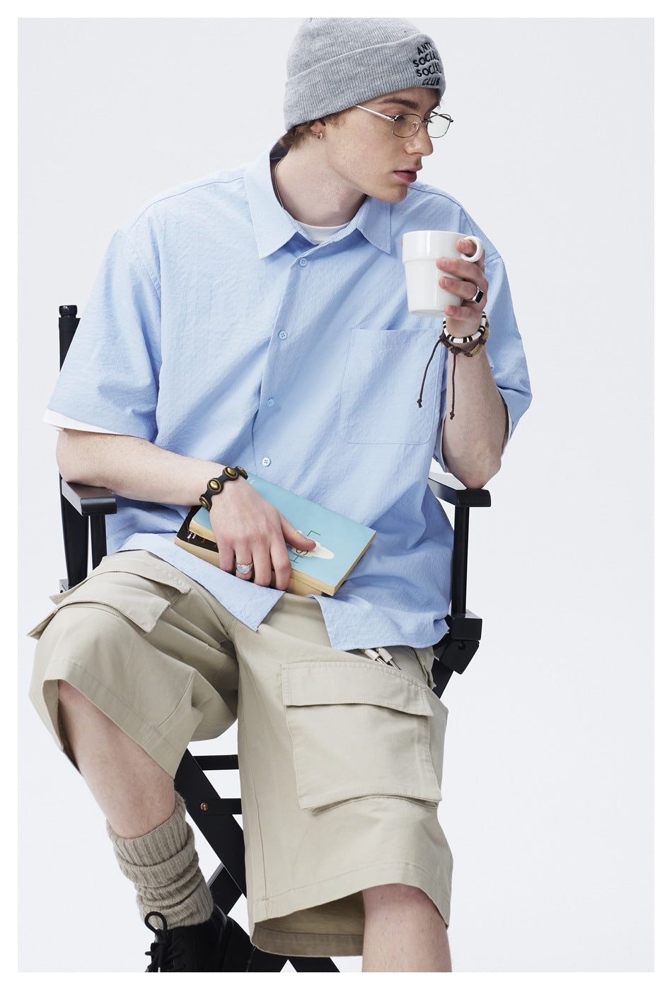 Seated model wearing a light blue short-sleeve button-up shirt with a chest pocket, shown from the front.