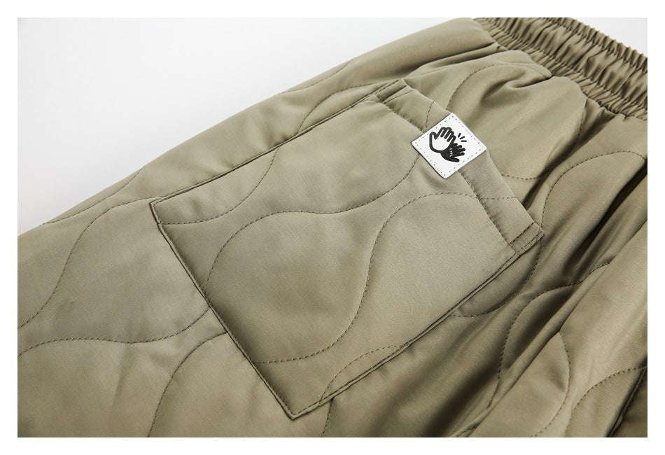 Close-up of a patch pocket and small hand-emblem label on olive-khaki quilted trousers.