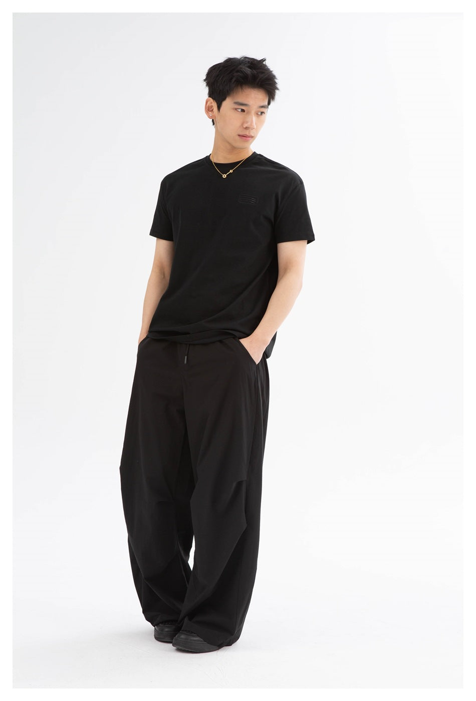 Model wearing a black short-sleeve T-shirt and loose black wide-leg trousers, shown from the front.