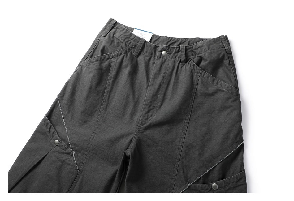 Cropped front view of charcoal utility pants with angled panel seams, snap-button tabs, and slanted pockets.