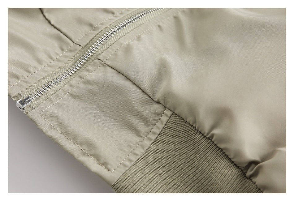 Close-up of a light khaki jacket showing a diagonal metal zipper, stitched seam, and ribbed hem.