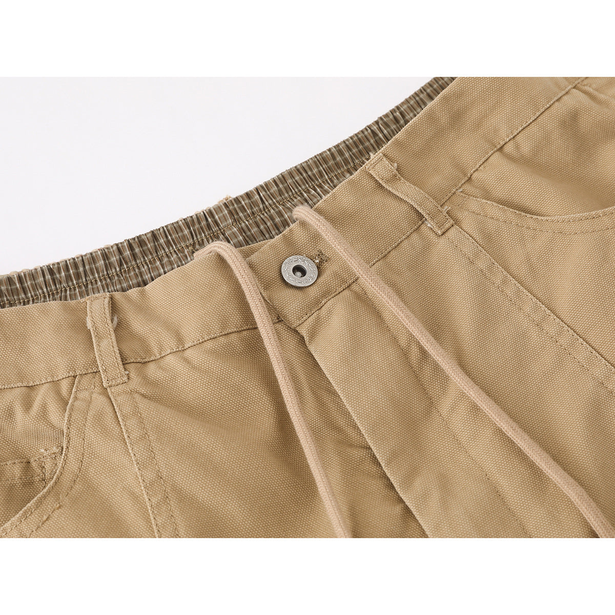 Close-up of tan trousers showing the elastic waistband, drawstring, button, and front pocket opening.
