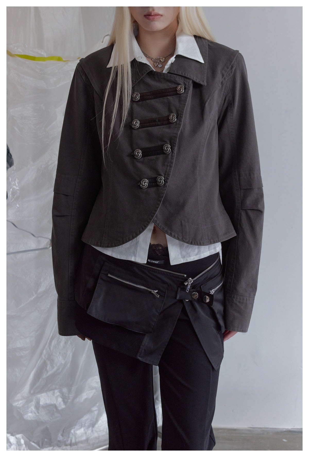 Close view of a model wearing a charcoal asymmetrical jacket with decorative loop fasteners over a white shirt.
