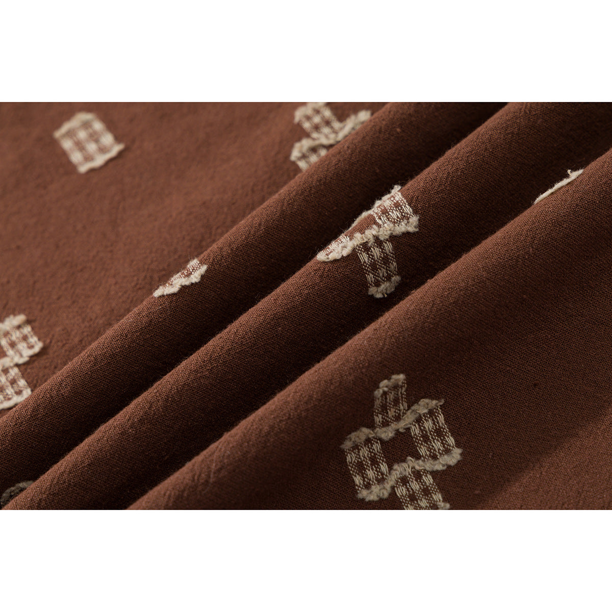 Macro view of brown fabric folds with cream geometric motifs and visible woven texture.