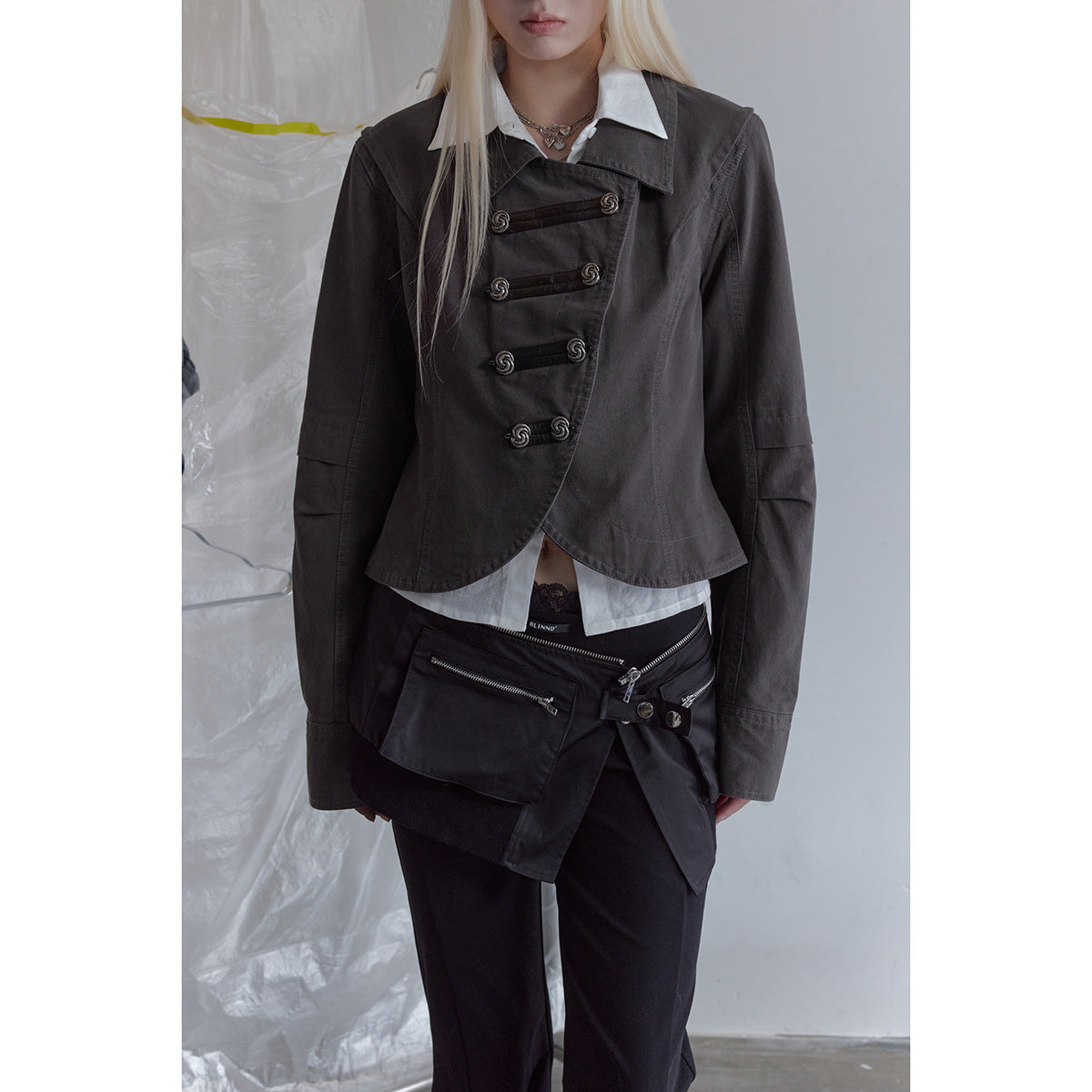 Cropped model wearing a charcoal asymmetrical jacket with loop fasteners over a white shirt and black trousers.