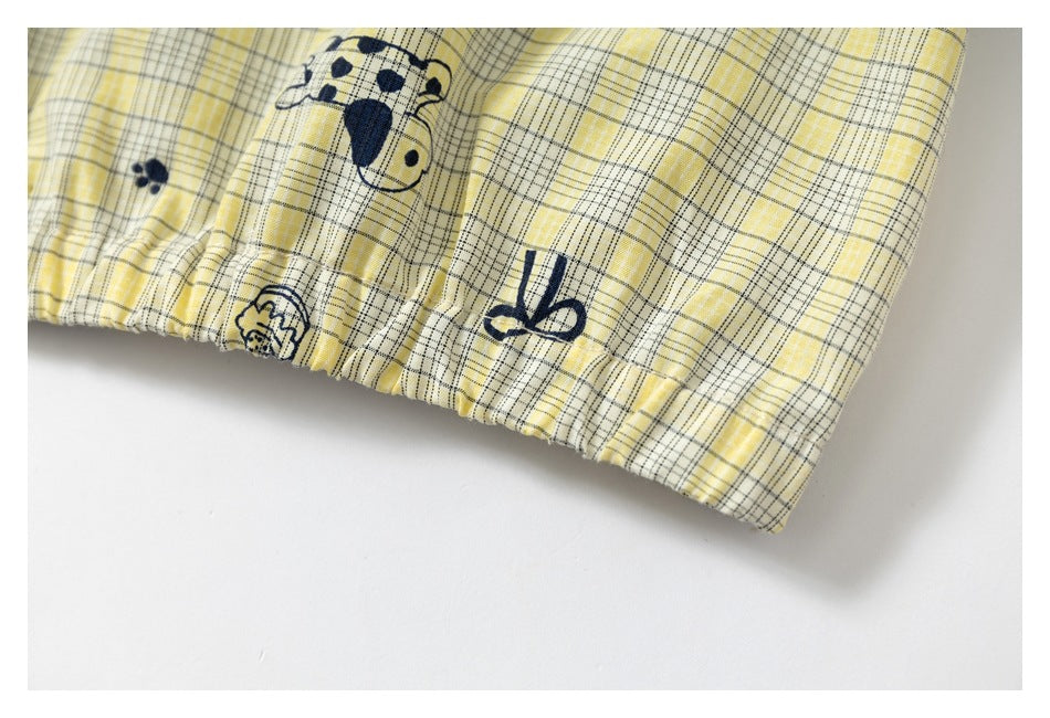 Close-up of a gathered hem on yellow plaid fabric, printed with navy dogs, paw prints, and bows.