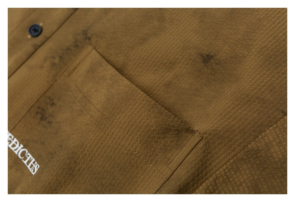 Close-up of a brown shirt's stitched chest pocket, textured fabric, and partial white lettering.