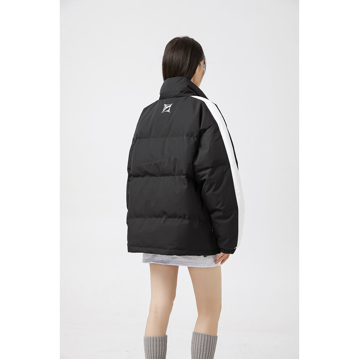 Back view of a model wearing a black padded jacket with white sleeve stripes and a small upper-back emblem.
