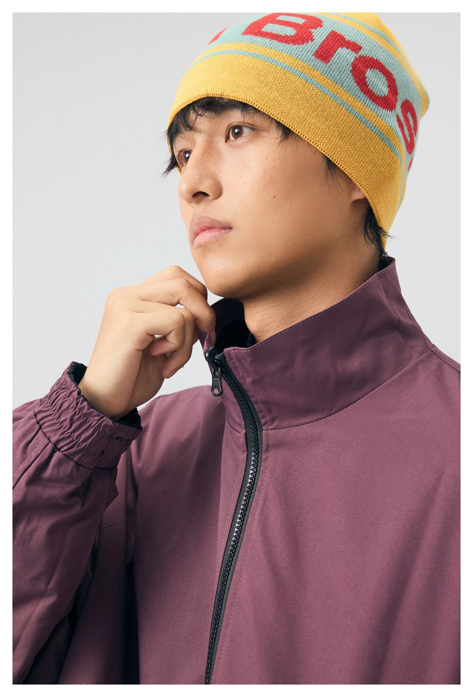 Close-up of a model wearing a plum jacket, showing its high collar and black front zipper.