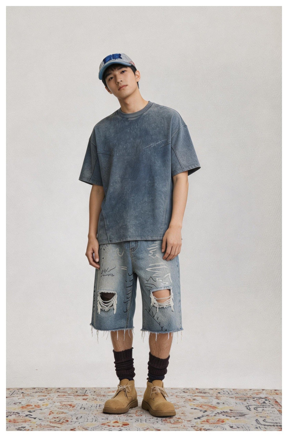 Model wearing a washed blue short-sleeve T-shirt with ripped denim shorts, a cap, socks and tan boots