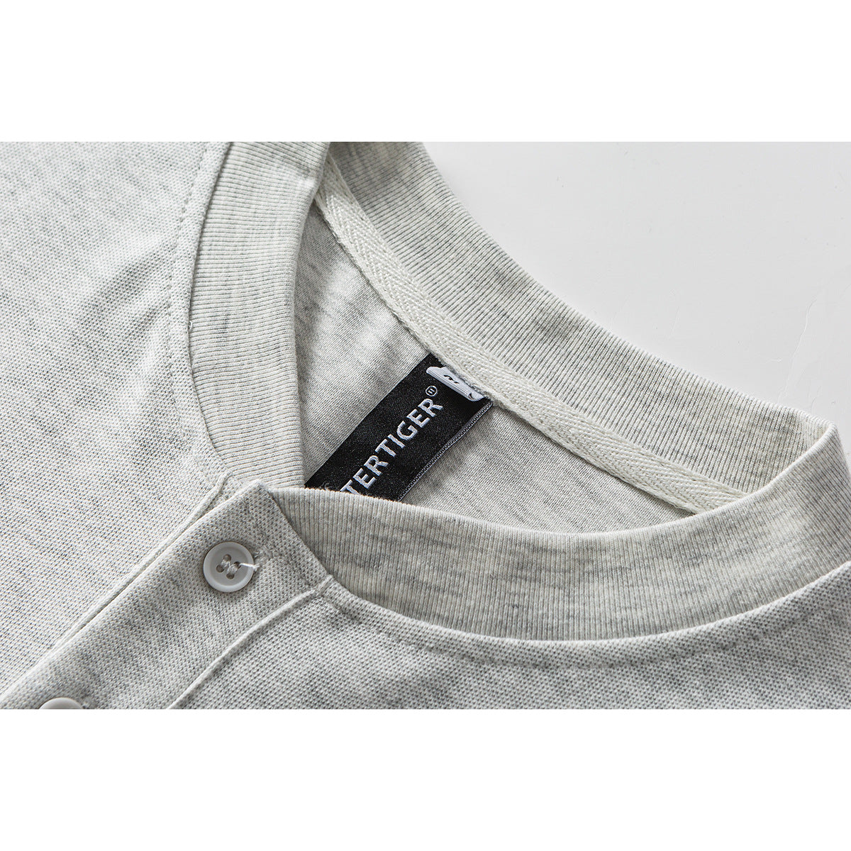 Close-up of a light gray shirt's ribbed collar, button placket, and black neck label.