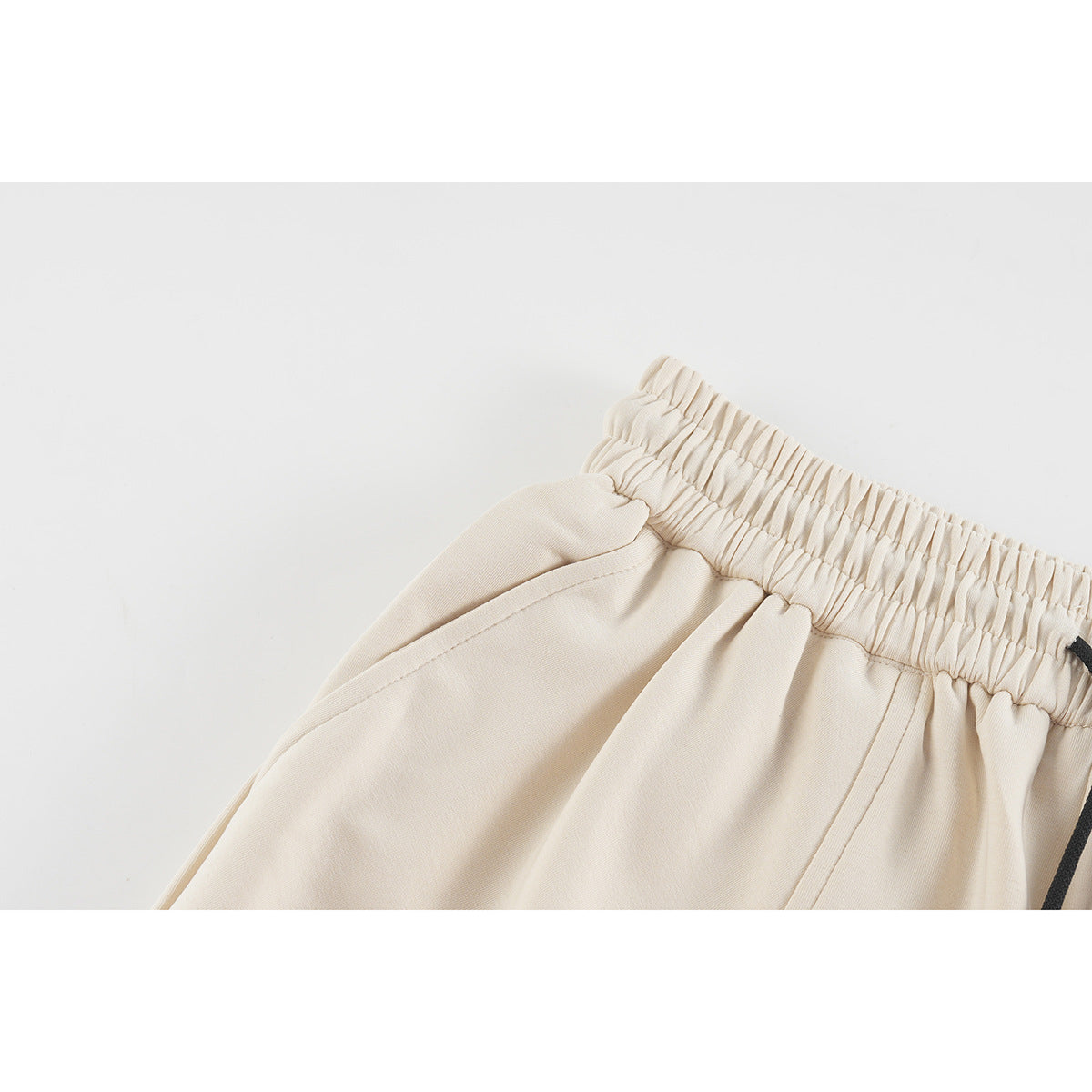 Close-up of cream shorts showing the gathered elastic waistband and curved side pocket seam.