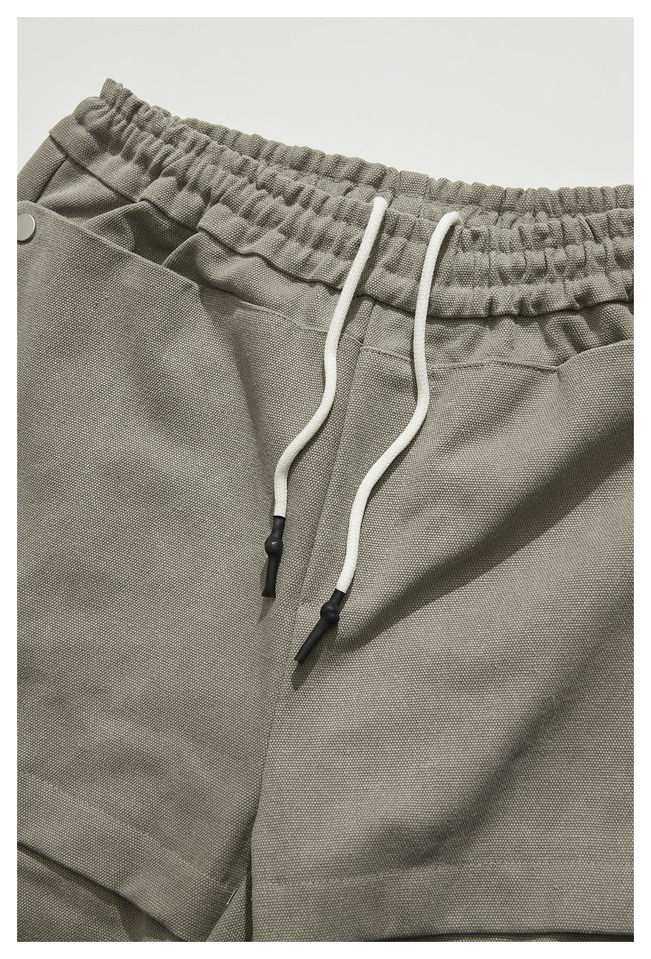 Close-up of gray-beige trousers with a gathered elastic waistband and long white drawstrings with black tips.