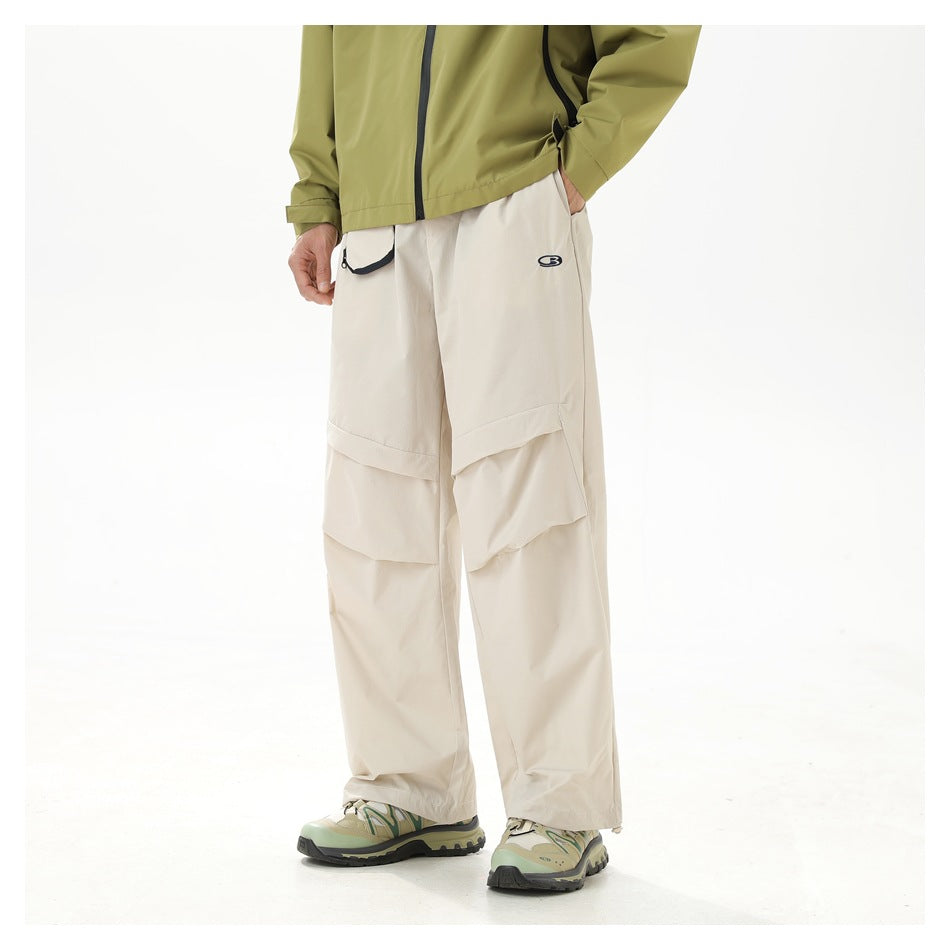 Cropped model wearing cream wide-leg cargo pants with layered knee panels and a small logo, shown from the front.