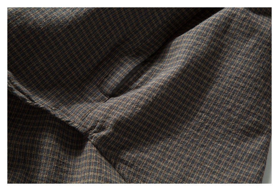 Close-up of a pocket opening and stitching on brown, blue, and tan checked fabric.