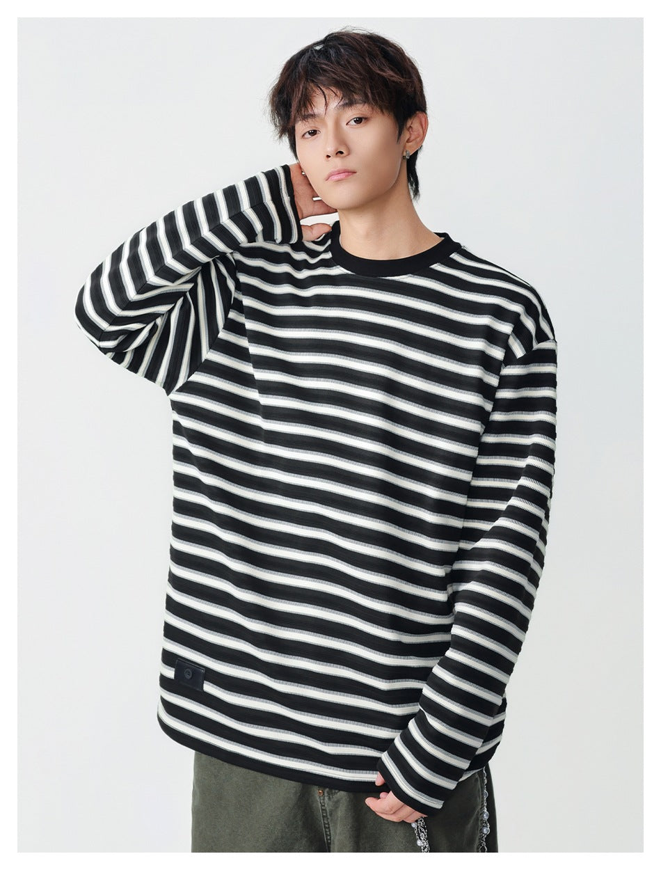 Model wearing an oversized black, gray, and white striped long-sleeve shirt with a black crew neck; front view.